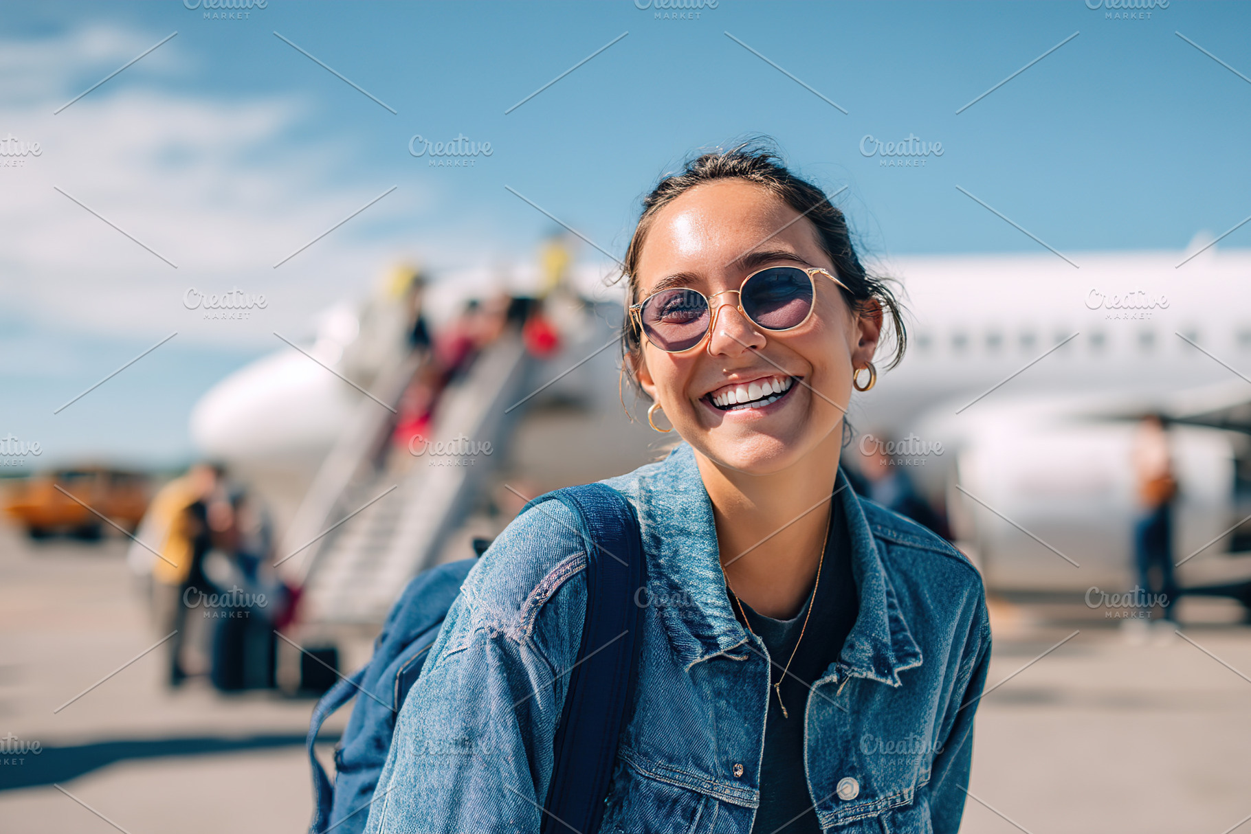 Laughing woman in denim jacket and sunglasses at airport enjoying travel moment, a Person Photo by AlyaAnd