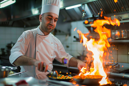 A chef focuses on cooking as flames, a Photo by Tanuart