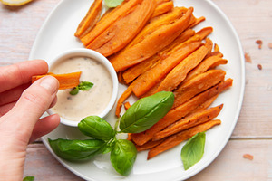 Hand dipping sweet potato fries in creamy sauce, a Food & Drink Photo by Olena Rudo
