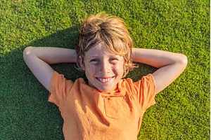 Boy lying on green grass looking at, a Nature Photo by Elizaveta Galitskaya