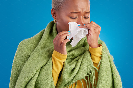 Sick black woman, tissue and blowing nose in studio, blue background or hayfever allergies, cold or winter virus. Female model, sneeze and influenza allergy of health problem, covid risk or sinusitis, a Photo by Peopleimages.com