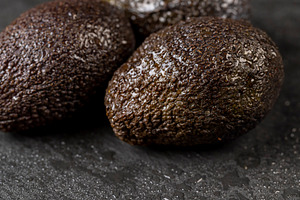 several wet whole black avocado fruits of small size on a black slate, a Photo by rsoollAI