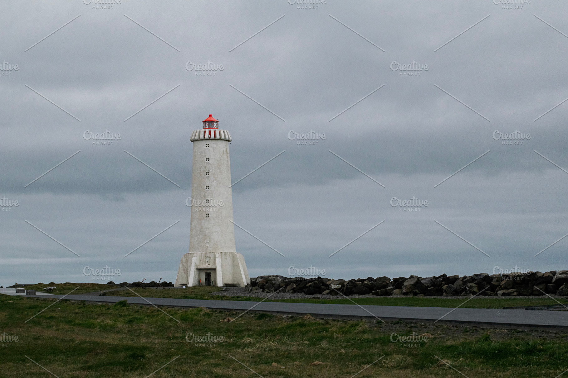 Lighthouse in Akranes, Iceland against a cloudy sky with rocky shoreline, a Photo by AS photostudio