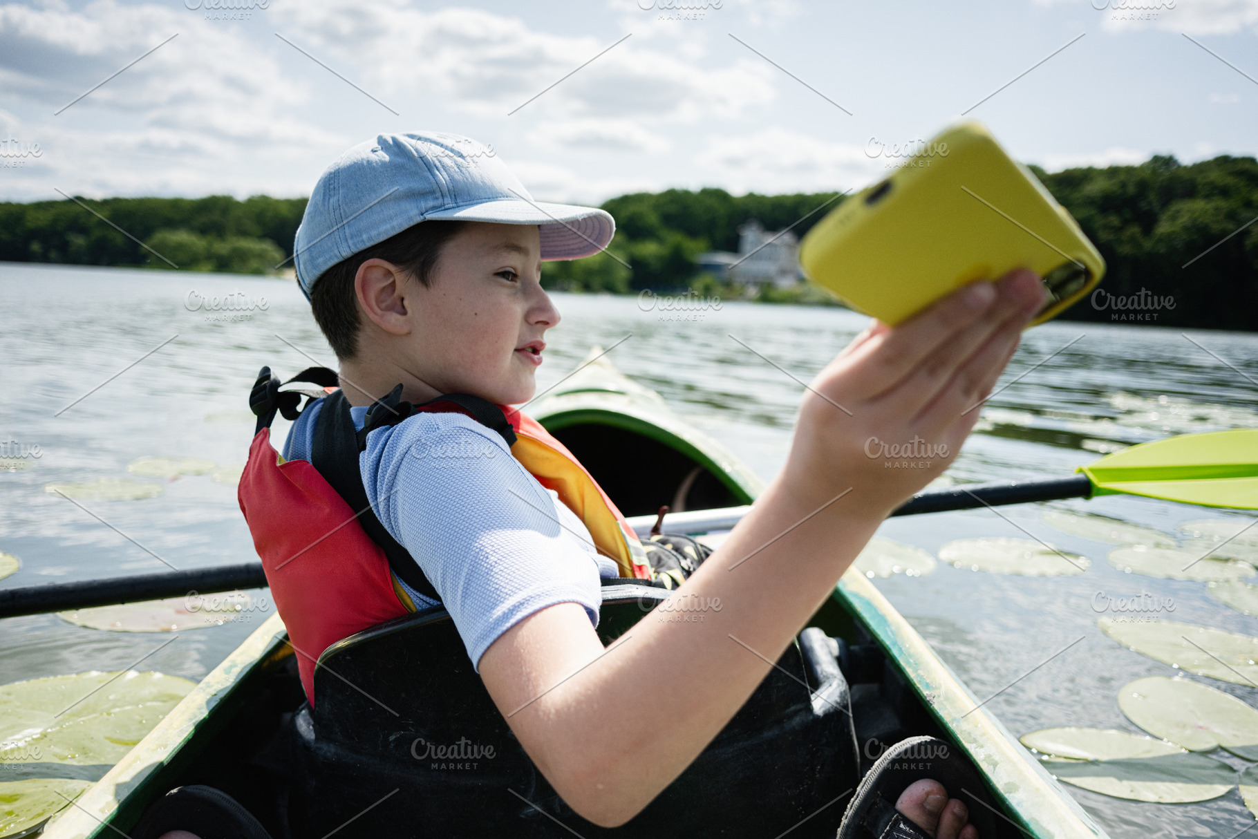 Young boy kayaking on a serene lake using a smartphone, a Photo by AS photostudio