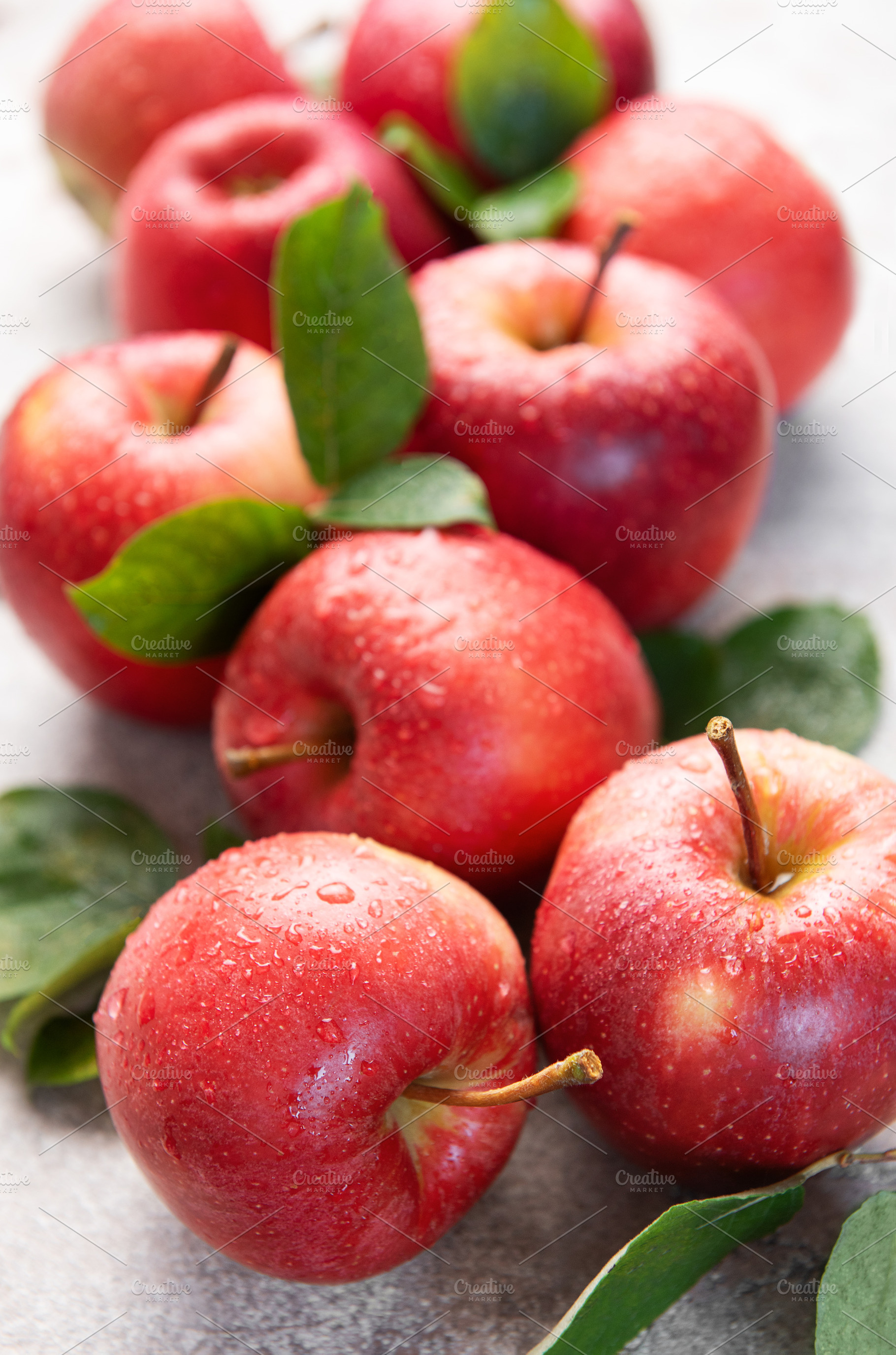 Fresh red apples with water drops and green leaves on gray backg, a Food & Drink Photo by Olena Rudo