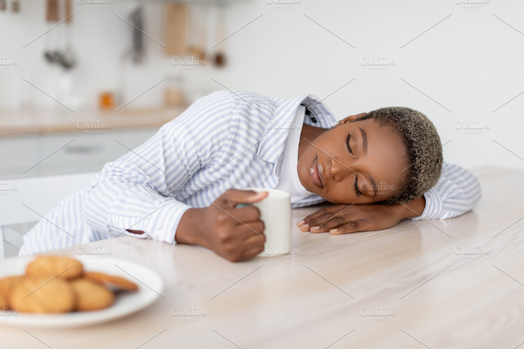 Tired young african american female with coffee cup sleeping on table in modern, a Person Photo by Prostock-Studio