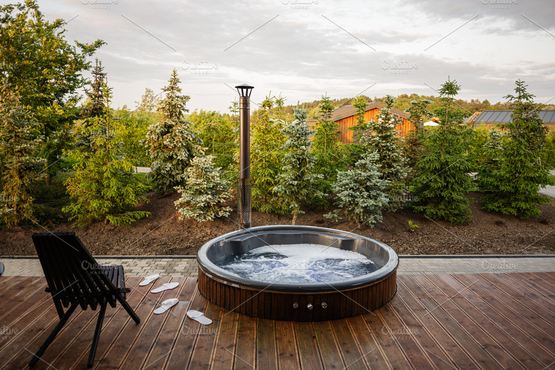 Outdoor hot tub on wooden deck surrounded by lush greenery under a cloudy sky, a Photo by AS photostudio