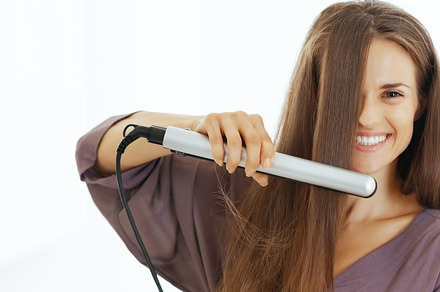 Happy young woman straightening hair in bathroom, a Person Photo by Alliance Images