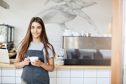 Portrait of young woman running a cafe and pastry shop standing near coffee machine looking at camera holding a cup of cappucino., a Person Photo by ringsaroundme