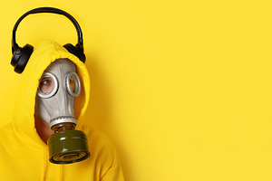 Person wearing a yellow hoodie, gas mask, and black headphones o, a Person Photo by Ales Munt
