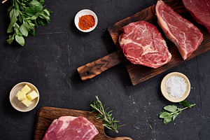 Raw rib-eye, flank, roast beef, and rump steak on wooden boards with spices and, a Food & Drink Photo by Asya Nurullina