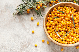 Sea buckthorn berries filling wooden bowl on table, a Food & Drink Photo by Olena Rudo