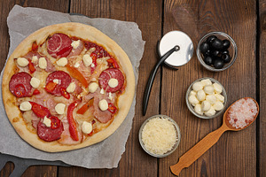 Pizza with salami, ham and mozzarella cheese on parchment, a Food & Drink Photo by ndanko