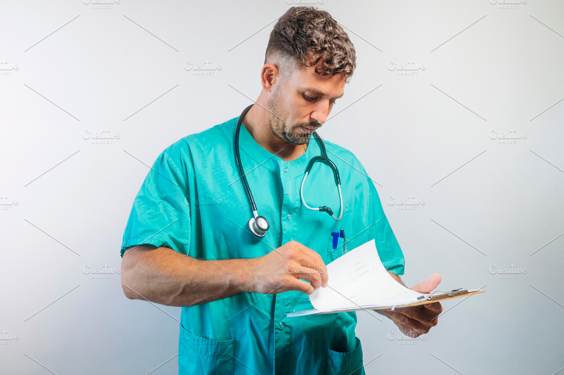 Focused male doctor reviewing documents on clipboard, wearing scrubs and stetho, a Person Photo by karrastock