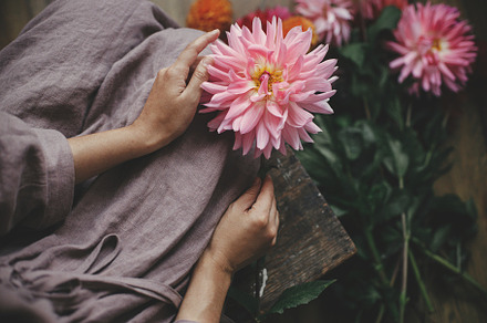 Woman in linen dress sitting on wooden rustic bench with pink da, a Holiday Photo by Sonjachni
