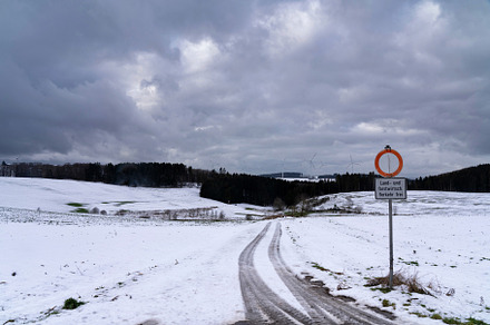 Snow-covered road leading to a forest under a dramatic cloudy sky in winter, a Nature Photo by John Stuij Photography