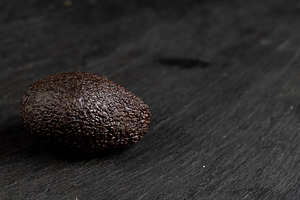 several whole black avocado fruits of small size on a black slate, a Photo by rsoollAI