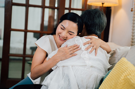 Asian daughter hugging mom on sofa
