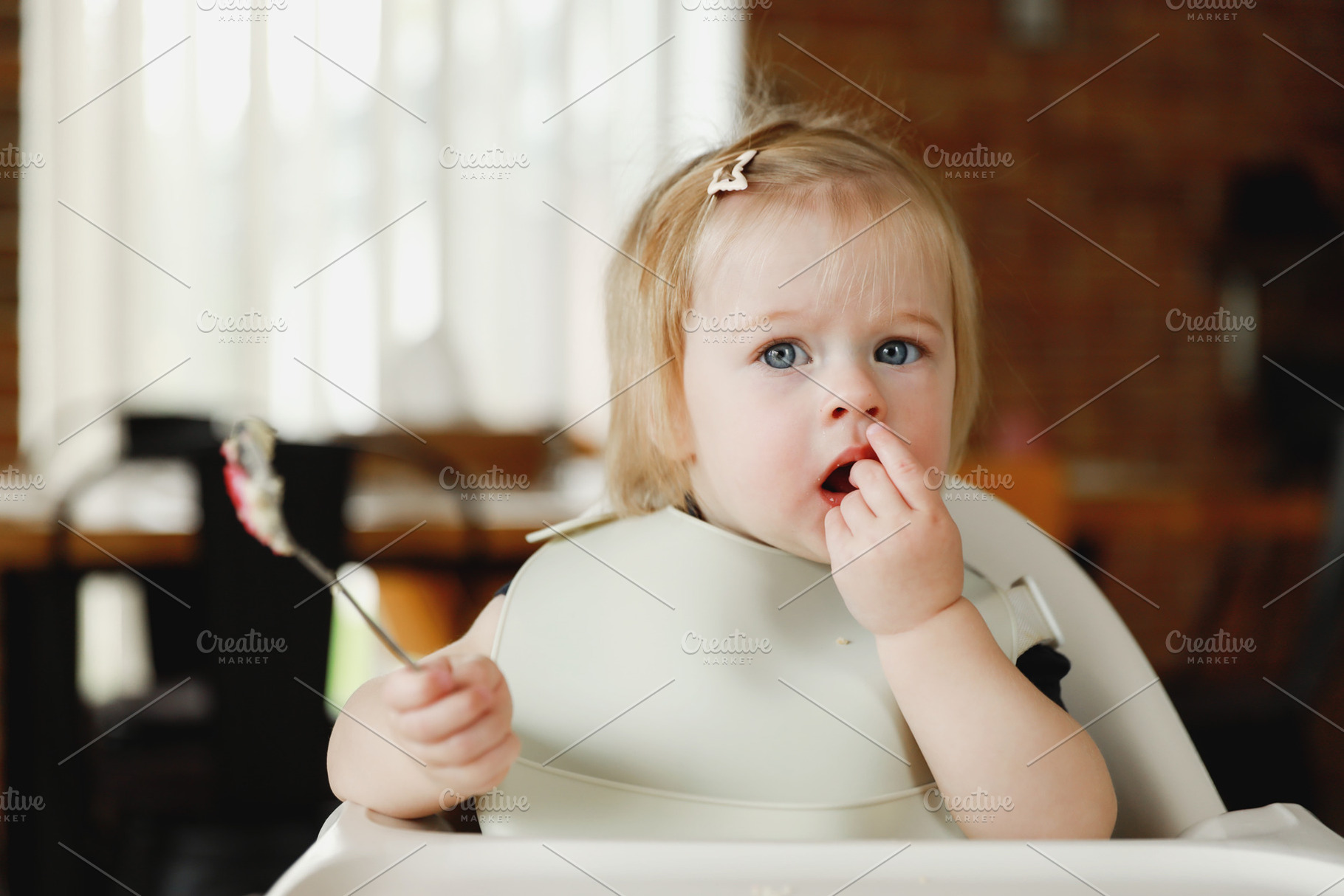 Infant girl or toddler sitting on high chair. Eating food by herself using spoo, a Person Photo by Lenor4ik