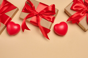 Gifts wrapped in red satin ribbon with a bow on a beige backgrou, a Holiday Photo by ndanko