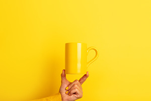 Hand in yellow sweater balancing a plain yellow ceramic mug on f, a Food & Drink Photo by Ales Munt