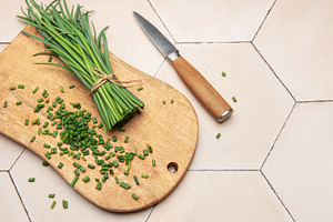 Freshly cut chives on wooden cutting board with knife, a Photo by Olena Rudo