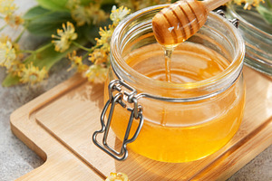 Golden linden honey jar with dipper on wooden board, a Food & Drink Photo by Olena Rudo