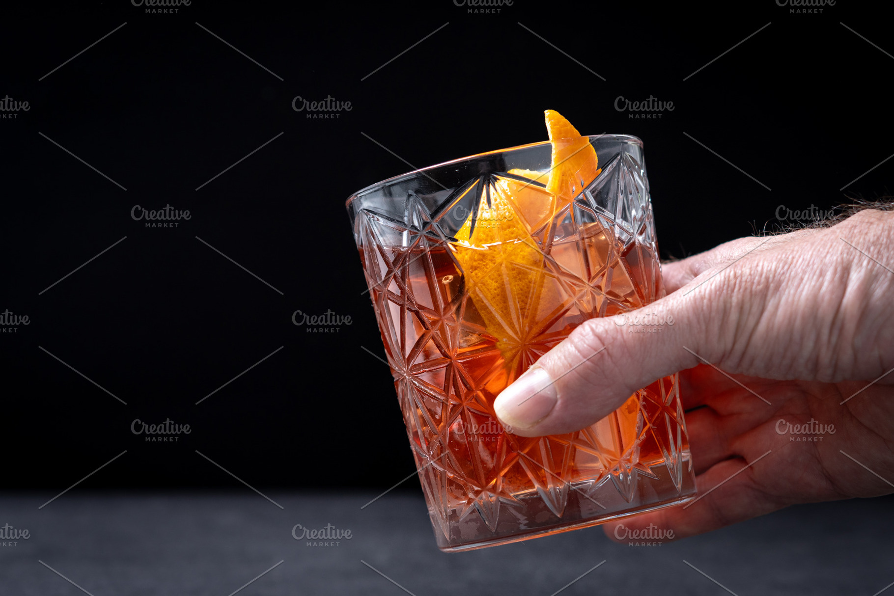 Hand holding classic old fashioned cocktail with orange garnish on dark backgro, a Food & Drink Photo by etorres69