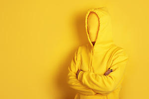 Faceless person in a yellow hoodie with crossed arms stands agai, a Person Photo by Ales Munt