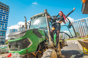 Joyful red haired woman raising hand on green tractor in modern, a Photo by Pictures for you!!!!!!!!!