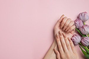 Woman showing nude manicure and purple tulips on pink background, a Beauty & Fashion Photo by Olena Rudo