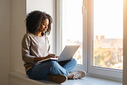 Student sitting by a window with a laptop and notebook, writing, a School & Education Photo by DanFLCreativo (Thumbnail 1 of 2)