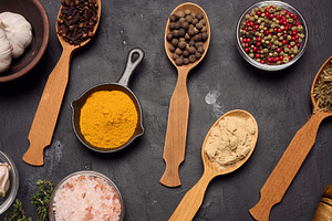Various ground spices in wooden spoons, olive oil on dark table, a Food & Drink Photo by ndanko
