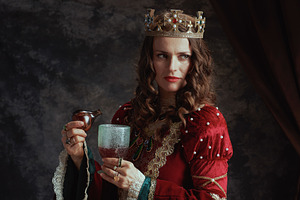 pensive medieval queen in red dress pouring poison into goblet, a Person Photo by Alliance Images