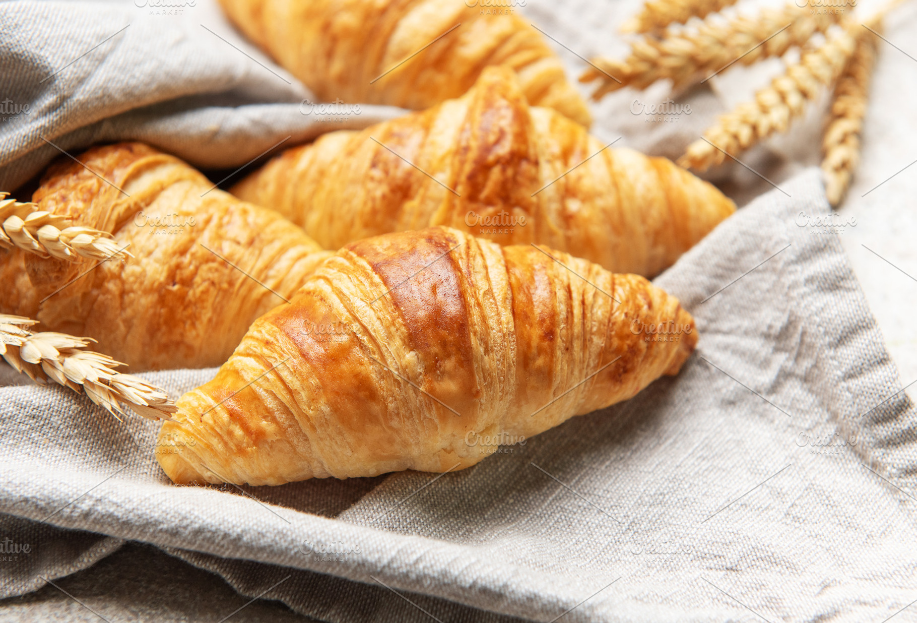 Freshly baked croissants resting on a linen cloth with wheat sta, a Food & Drink Photo by Olena Rudo