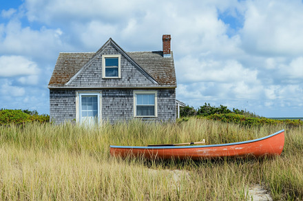 A quaint wooden cape cod house with a gray shingle exterior sits amidst tall gr, an Architecture Photo by Textures & Backgrounds