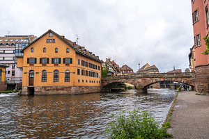 Yellow riverside building and stone bridge in Strasbourg, France, an Architecture Photo by GoodGoods