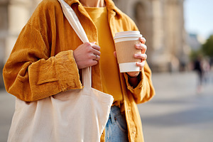 Holding a reusable coffee cup and cloth bag while exploring a city street in th, a Food & Drink Photo by AlyaAnd