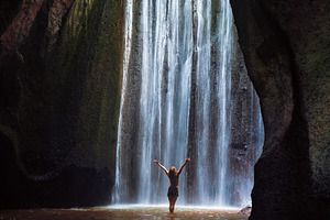 Woman stand under cave waterfall featuring bali, travel, and indonesia