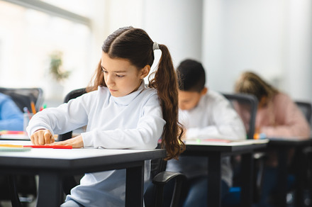 Portrait of small girl sitting at desk in classroom, a Photo by Prostock-Studio