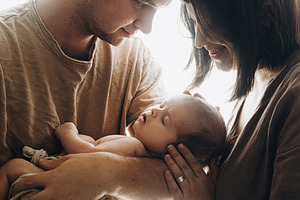 Happy mother and father hugging little baby son in window light., a Person Photo by Sonjachni