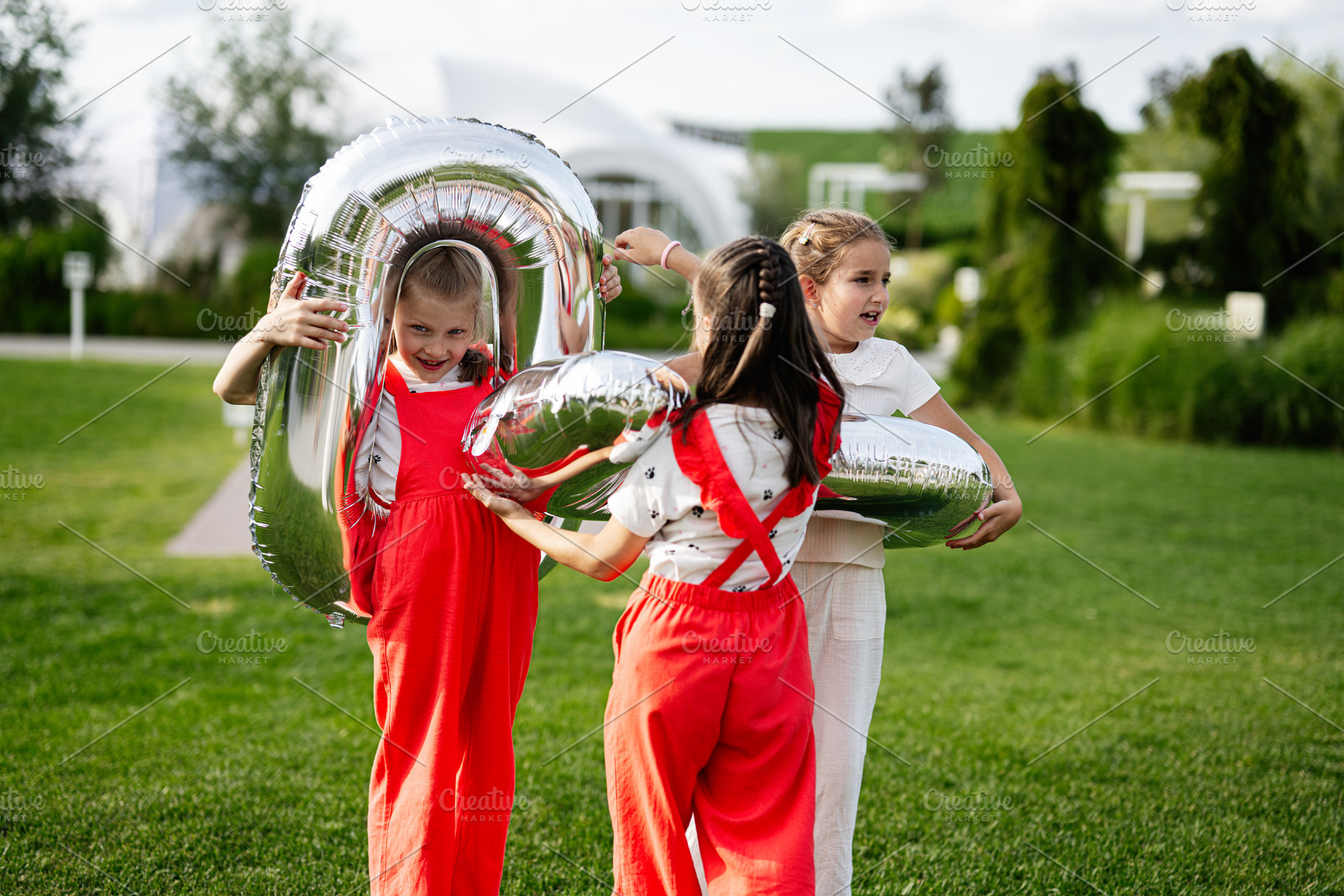 Three children playing with balloons outdoors on a sunny day in a park, a Photo by AS photostudio