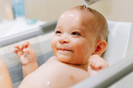 Portrait of a nine month old baby taking a bath with water running trough his f