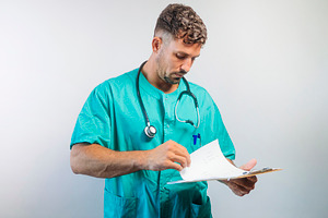 Focused male doctor reviewing documents on clipboard, wearing scrubs and stetho, a Person Photo by karrastock