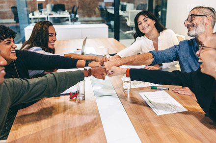 Cheerful businesspeople bringing their fists together in a boardroom, a Person Photo by Jacob Lund