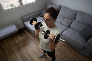 Woman doing triceps exercise with dumbbell at home, a Person Photo by etorres69