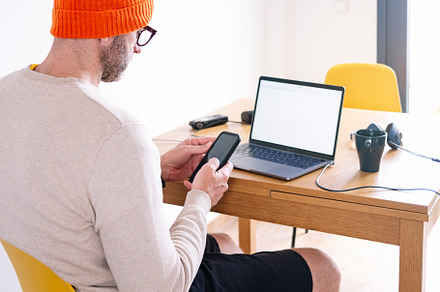 Man working from home on a laptop and smart phone sitting at a desk surfing the, a Person Photo by karrastock