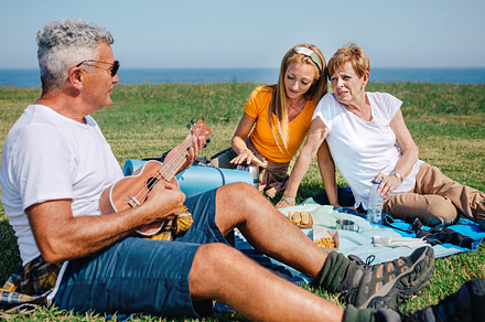 Senior man playing ukulele for his family sitting on a blanket during an excurs, a Holiday Photo by davidpereiras