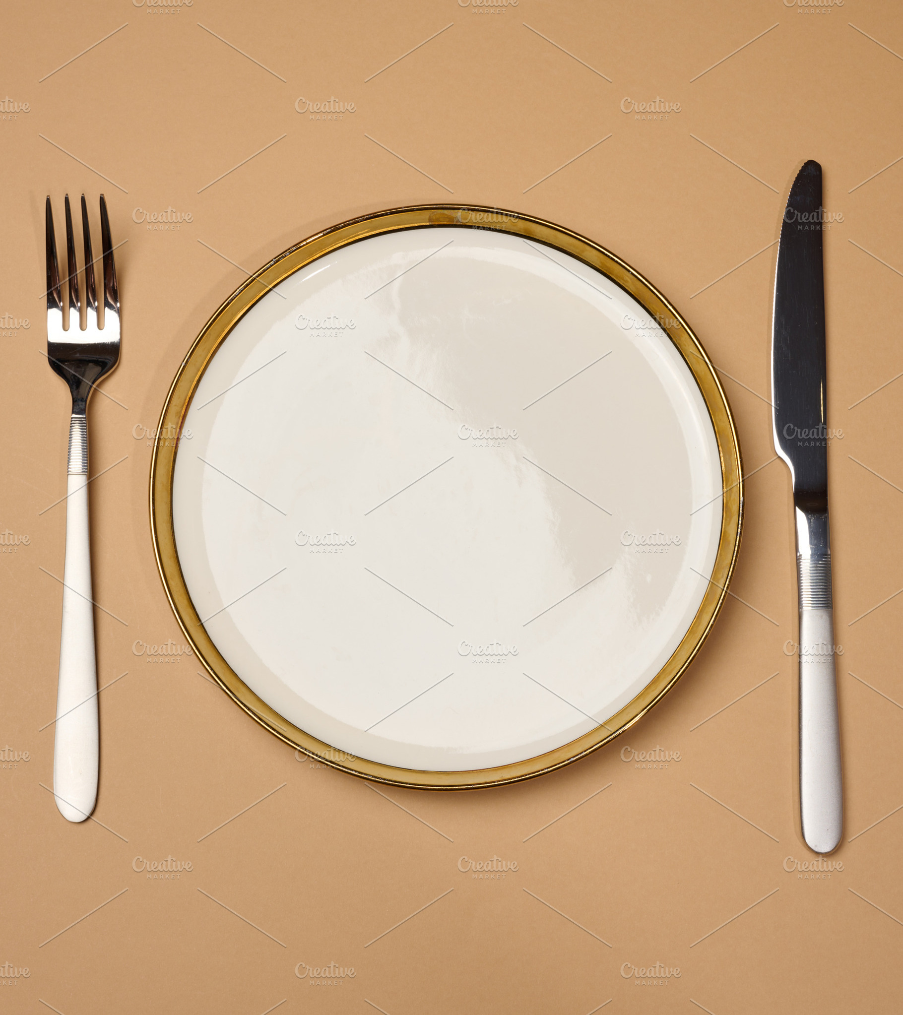 Round white empty ceramic plate and knife with fork on brown bac, a Food & Drink Photo by ndanko