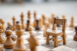 Chess table featuring a wooden chair amidst intricately carved chess pieces dur, a Photo by AlyaAnd